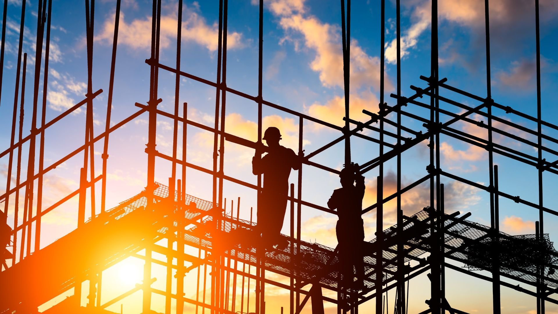 Construction workers on scaffolding silhouetted against dramatic sunset sky