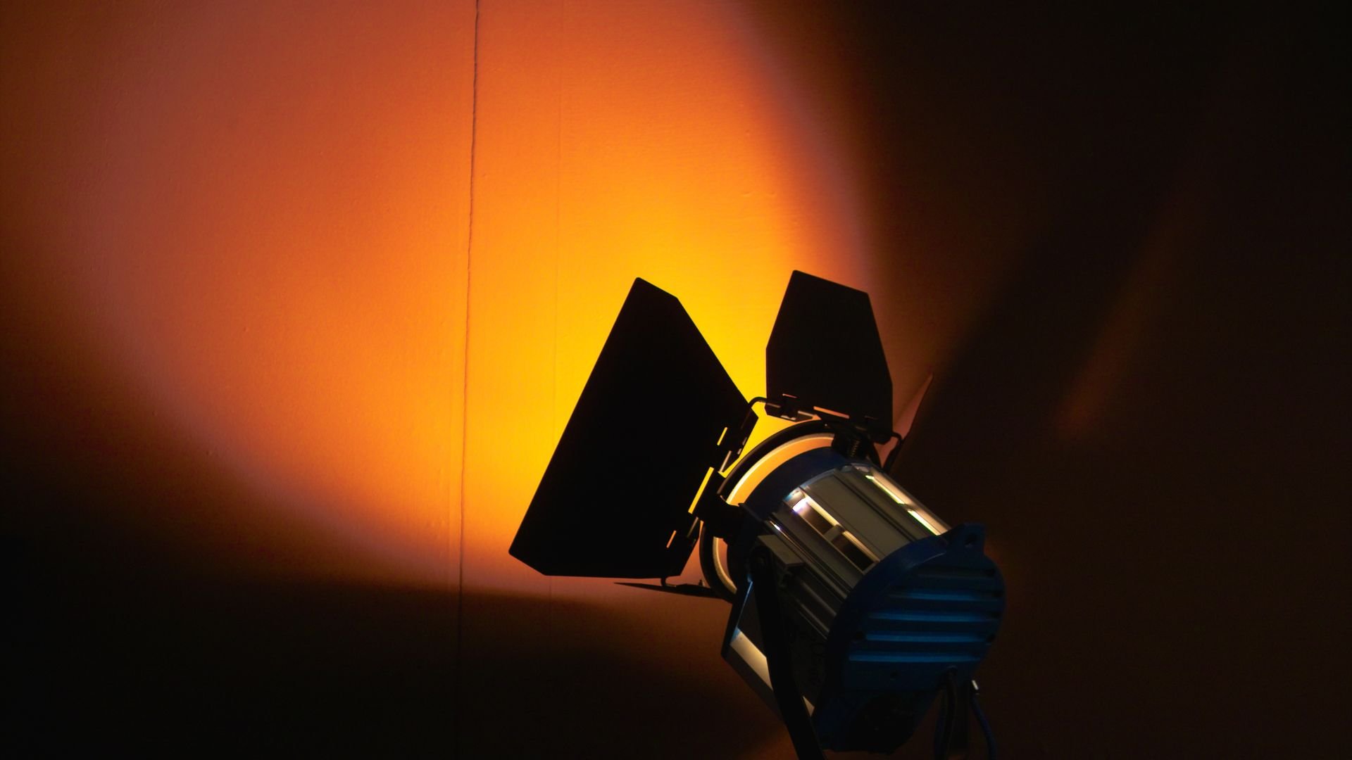 Studio light with barn doors casting warm orange glow on dark background