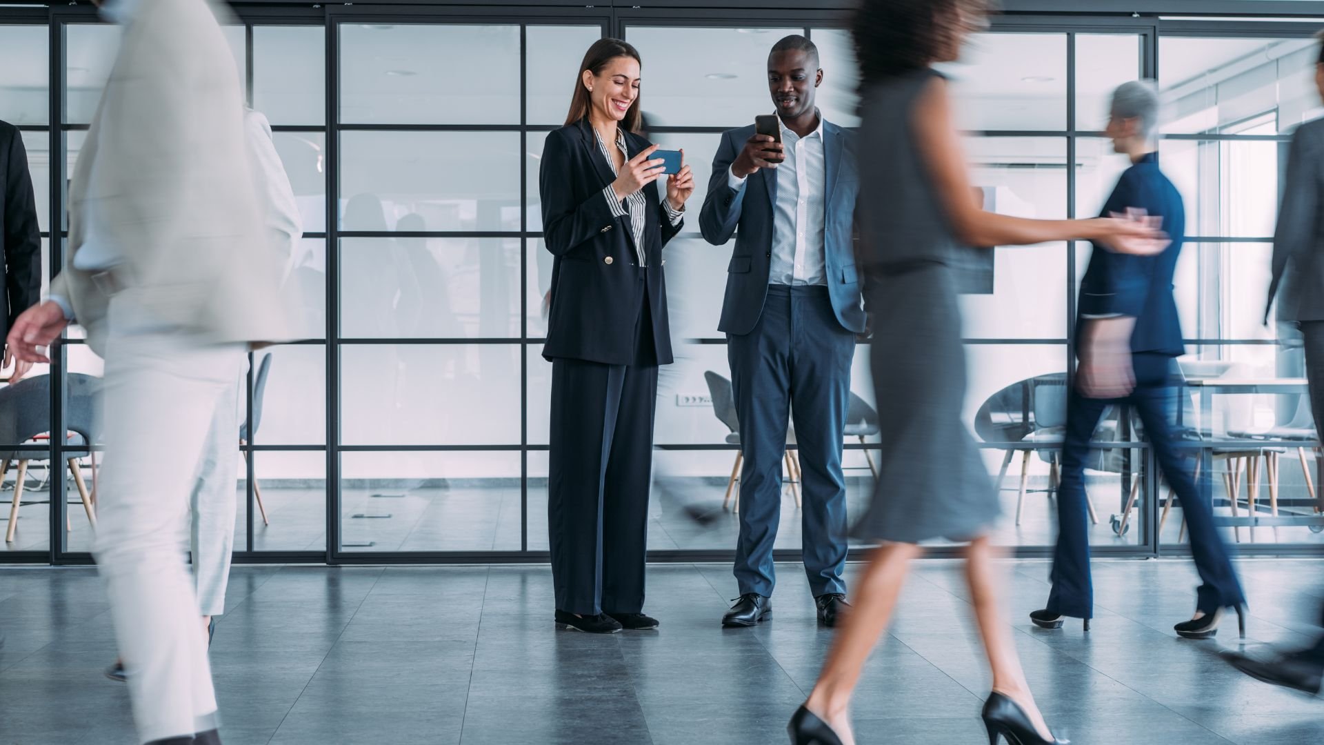 Business professionals using smartphones in modern glass office with blurred movement