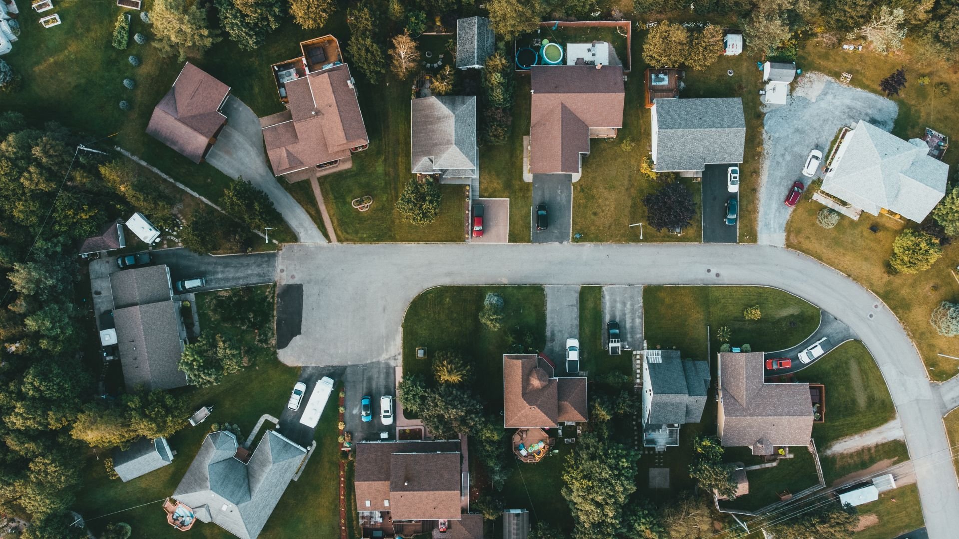 Aerial view of suburban neighborhood with houses, driveways, and parked cars