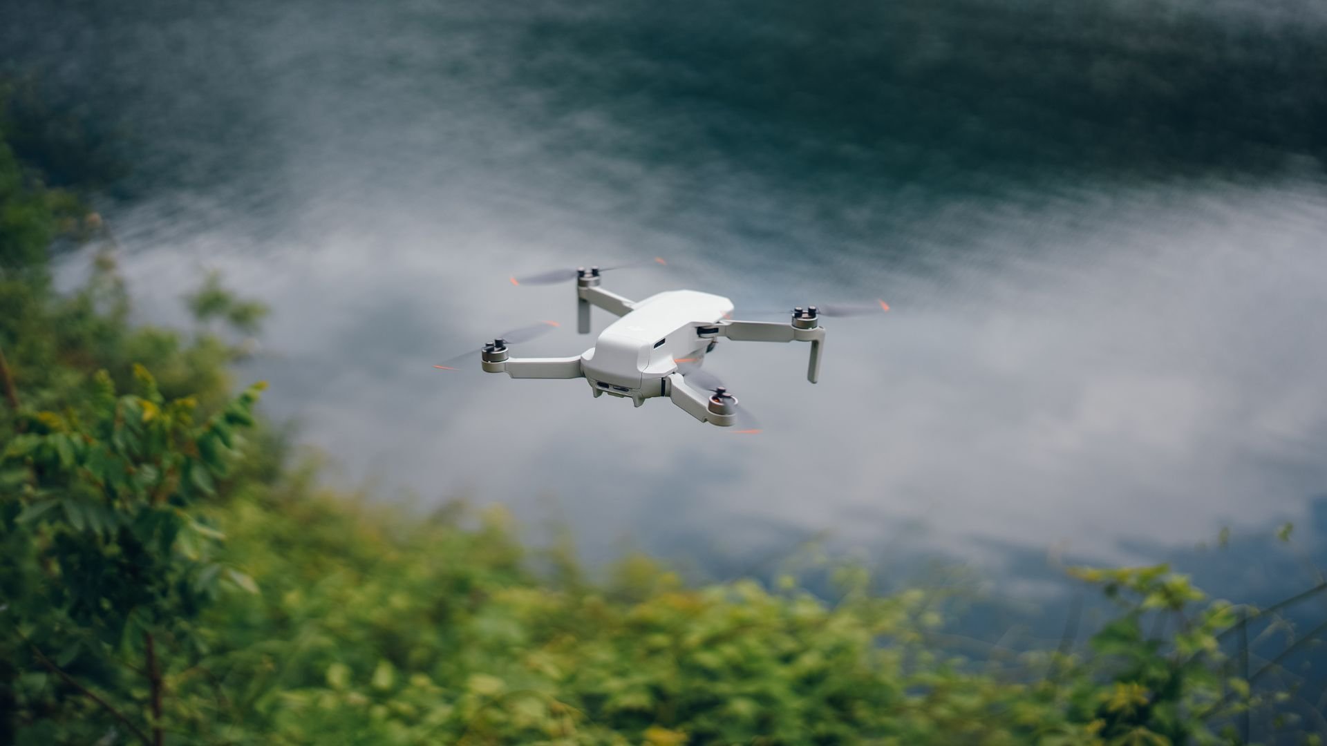 White drone flying over misty green forest landscape